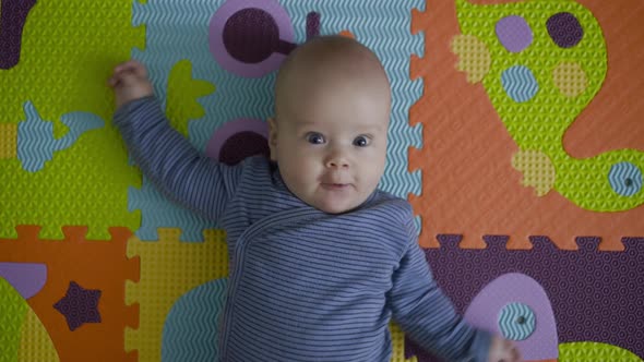 Joyful Newborn with Outstretched Arms Lying on Carpet and Looking at Camera