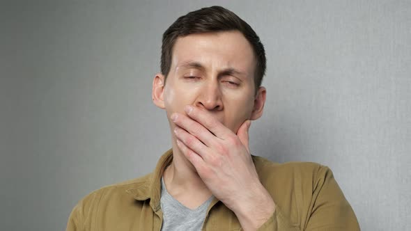 Young Man Yawns Standing Against Grey Wall