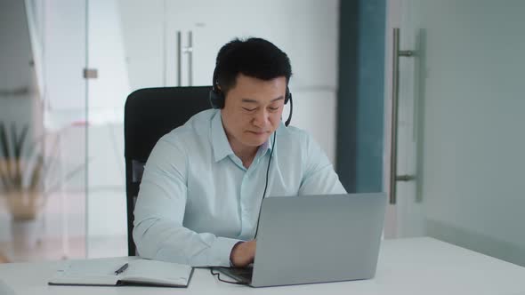 Confident Middle Aged Asian Businessman Wearing Headset Video Conferencing with Partners Online Via