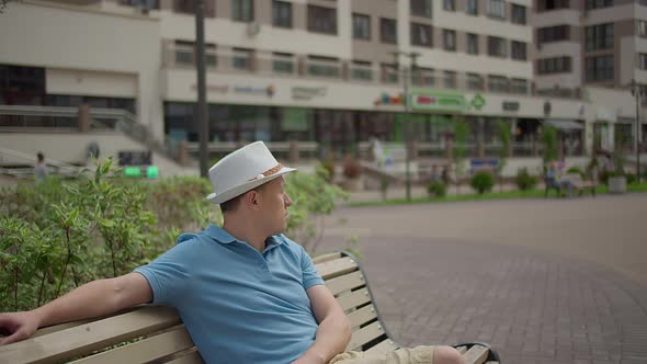Man in a Hat Sits on a City Bench Resting While Walking Around the City Camera Movement