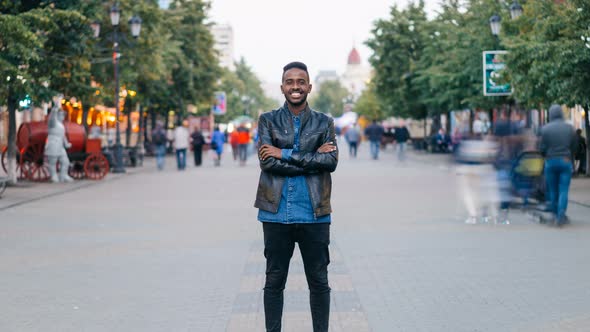 Zoom in Time-lapse of Happy African American Guy Wearing Jeans and Leather Jacket Standing Alone in