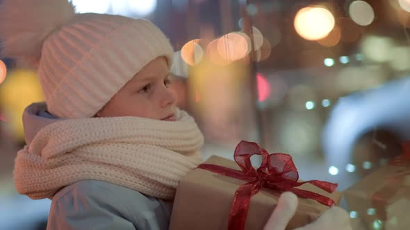 Portrait Boy with Gifts Box Looking and Dreaming in Christmas Window Shopping on Traditional