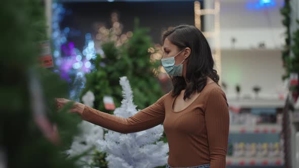 A Woman in a Protective Mask in a Jewelry Store and Garlands with Toys for Christmas Trees and at