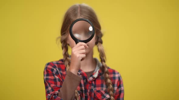 Teenage Girl with Magnifier Looking Around Standing at Yellow Background