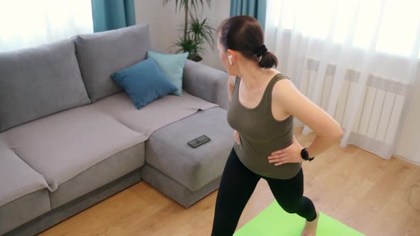 A Woman in a Tshirt Black Leggings is Doing Exercises on a Rug in a Bright Room