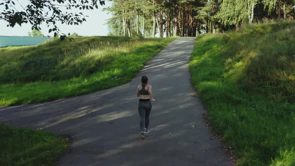 Young Attractive Girl Running in City Park. Woman Running in Wood Aerial Back View. , Tracking Shot.