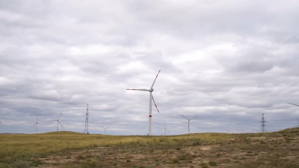 Motion the Blades of a Large Wind Turbine in a Field Against a Background of Cloudy Grey Sky on the