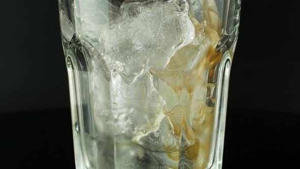 Pouring cola with ice cubes close-up. Cola with Ice and bubbles in glass on a black background.