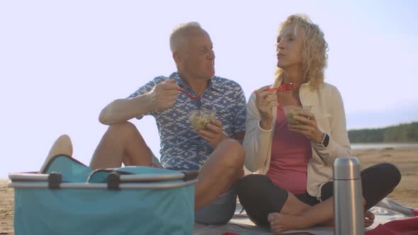 Senior Happy Couple on Picnic Eating Salad Relaxing on Sea Beach