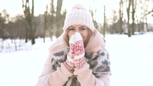 Young Woman in a Soft Pink Down Jacket White Hat Mittens and Scarf on a Background of Snowy