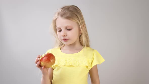 Girl with an Apple. Little Girl Eating an Apple Girl in a Yellow Bright Dress on a White Background.