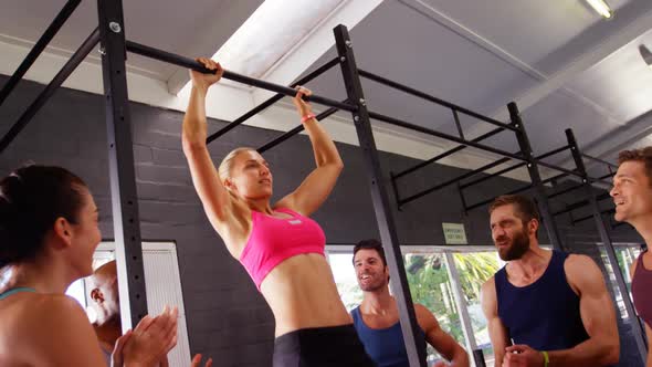 Women performing pull-up exercise while friends applauding her