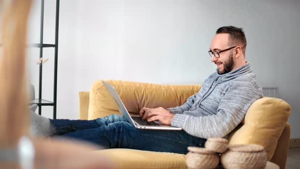 Cheerful Male Freelancer Working Remotely Surfing Internet on Laptop on Couch