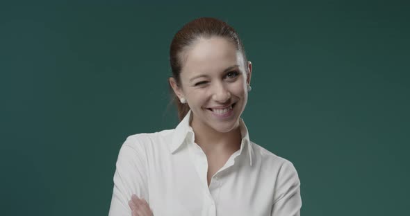 Cute young woman winking and smiling at camera with arms crossed