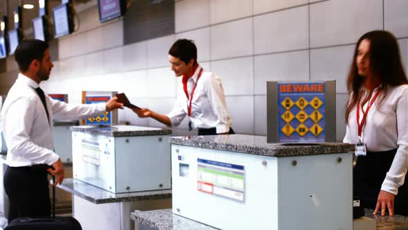 Two female airport staff checking passport and interacting with commuters at check-in desk