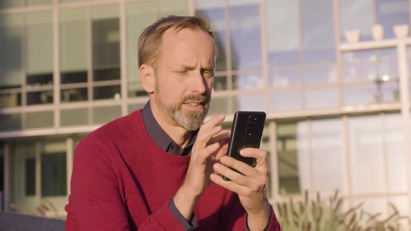 A Middleaged Handsome Caucasian Man Works on a Smartphone with a Smile As He Sits