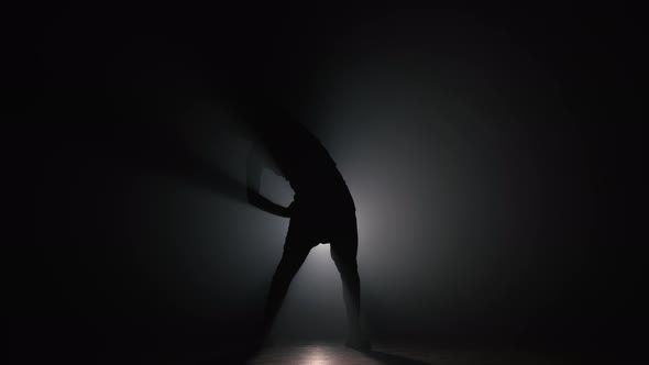 Silhouette of Young Man Warming Up Before Training in Dark Studio with Smoke. Workout in Gym