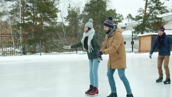 Happy Couples Ice-skating in Park Holding Hands Laughing Having Fun Together