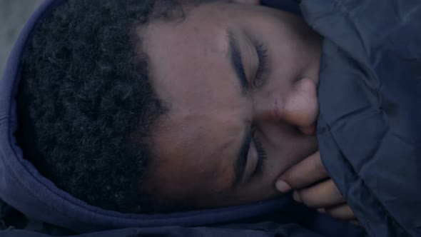 Close-up of bruised black teen boy lying on street and coughing