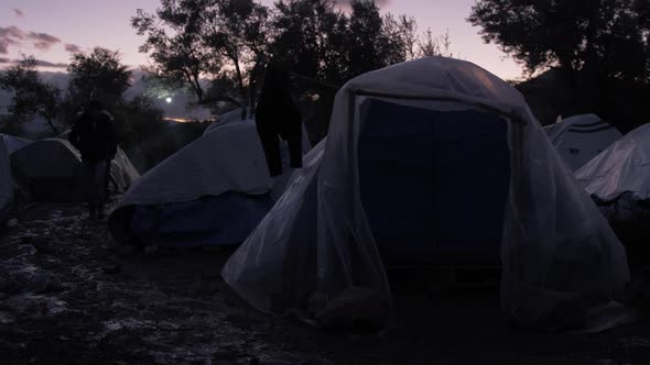 A refugee silhouetted at dusk walks around tents Moria Refugee Camp