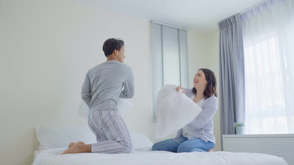 Asian young beautiful loving couple enjoy early morning activity, have pillow fight together on bed.
