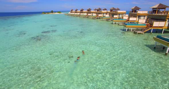 Aerial drone view of a man and woman couple with seascooters snorkeling near overwater bungalows.
