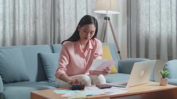 Asian Woman With A Laptop Holding Bill And Calculating Money By Calculator Then Having A Headache