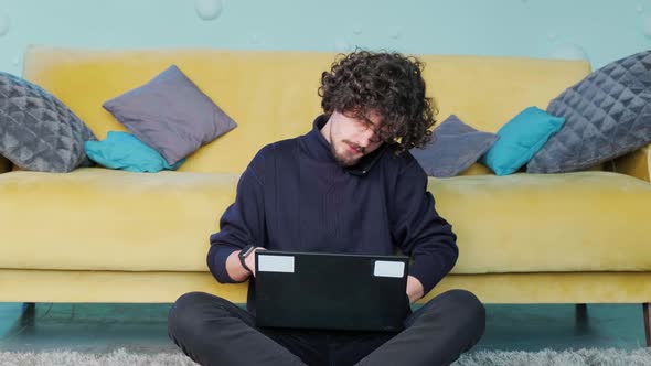 Young Man Talks on the Phone and Works at the Computer While Sitting on the Floor