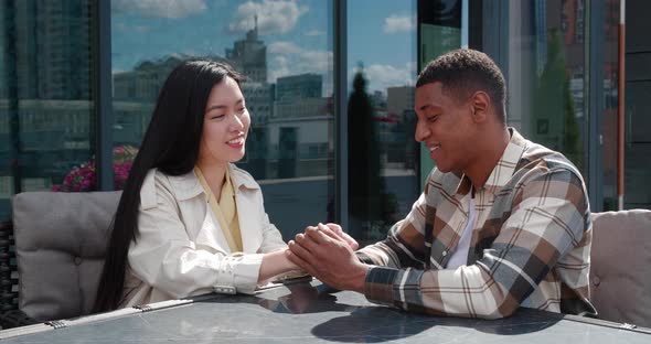 Beautiful Asian Woman and Handsome African Guy Sitting Together at a Table on the Cafeteria Terrace