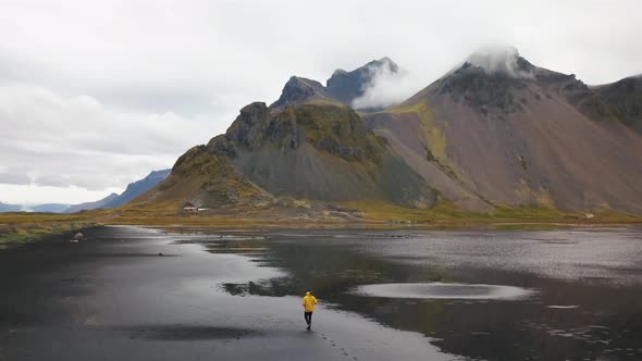 a photographer wearing a yellow jacket walking in hofn beach