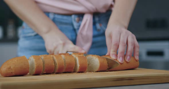 Woman Skillfully Cutting Homemade Bread on Cutting Board on Kitchen Table