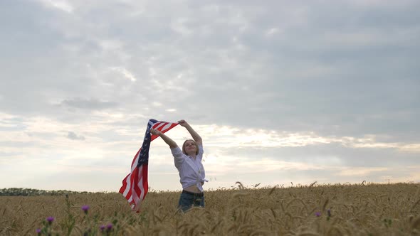 Happy Patriotic Young Woman Waves the US Flag Into the Field