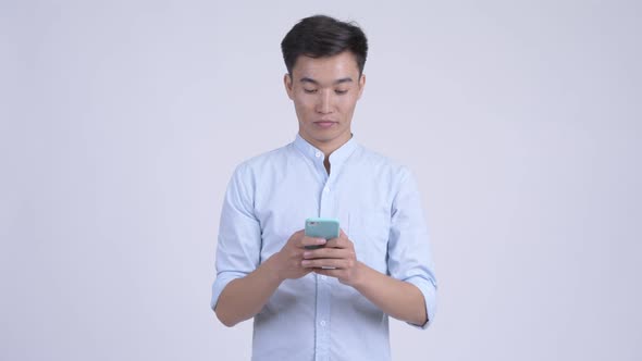Young Happy Asian Businessman Thinking While Using Phone