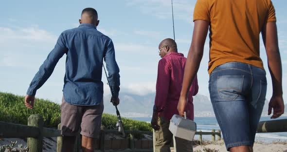 African american senior father and two teenage sons standing on a beach fishing and talking