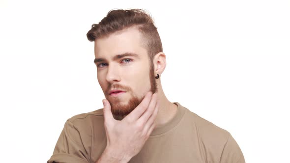 Handsome Young Caucasian Standing on White Background Touching Hair and Beard