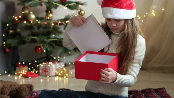 Little Girl in Santa Hat Opens a Christmas Gift and Gets Upset