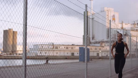 Young Woman In Sportswear And Headphones Running Along Harbour