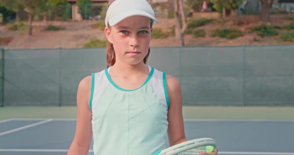 Young Tennis Player Looks Into the Camera While Holding Her Colorful Racket