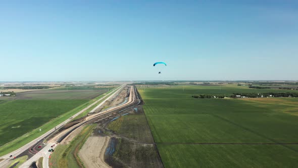 Lone paragliding flying over rural agricultural farm field landscape
