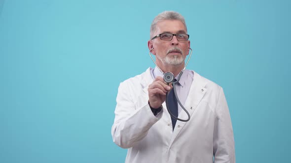 An Adult Doctor Pretends to Listen with Stethoscope in the Studio a Blue Background