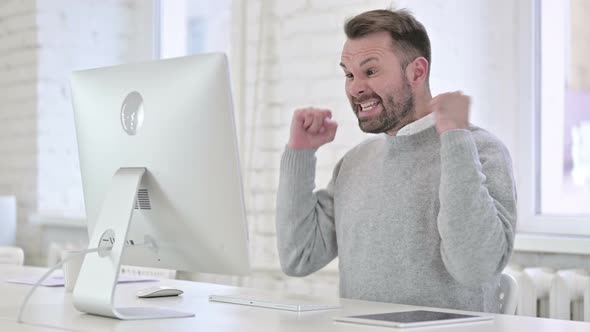 Excited Young Man Celebrating Success on Desktop