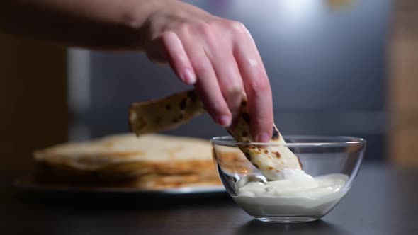 girl twists a pancake into a tube and dips it in sour cream