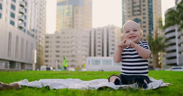 Happy Small Child Sitting in Grass with White Daisies City Background