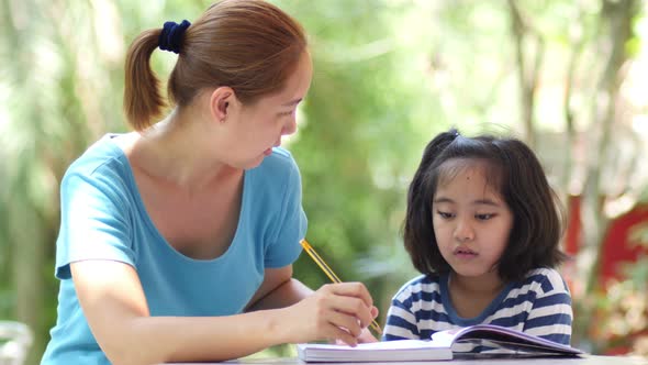 Little Asian girl with mother doing homework on the table, Pan shot