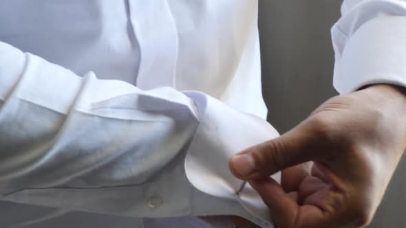 Close-up of a groom's wrists as he puts a cuff link on his sleeve in preparation for marriage