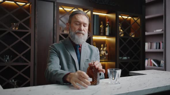 Rich Wealthy Mature Successful Bearded Businessman Pouring Portion of Aged Whiskey Into Glass