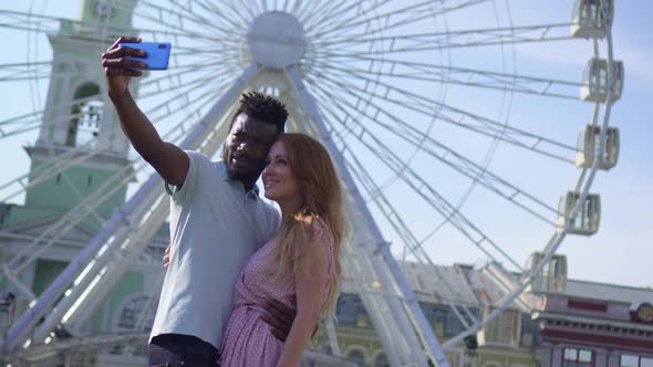 Young Couple Makes Selfie on the Background of a Ferris Wheel