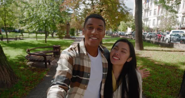 Happy Multiracial Young Loving Couple Actively Walking in the Park and Recording Video or Having