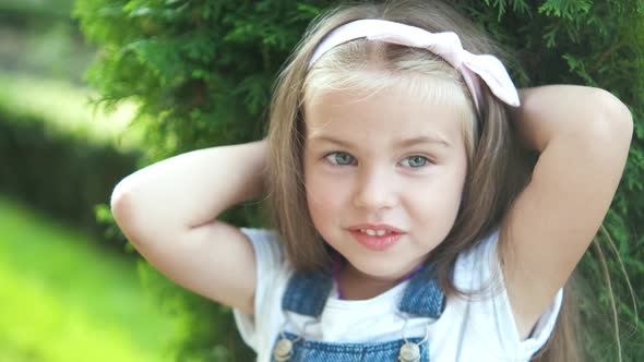 Portrait of pretty child girl standing in summer park looking in camera smiling happily.