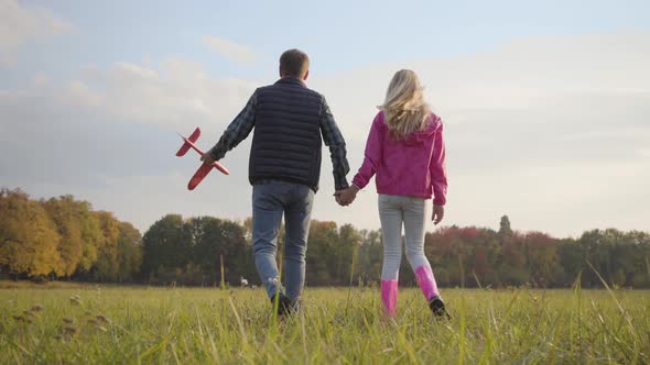 Back View of a Caucasian Man Holding Hand of Teen Blonde Girl and Pink Toy Airplane